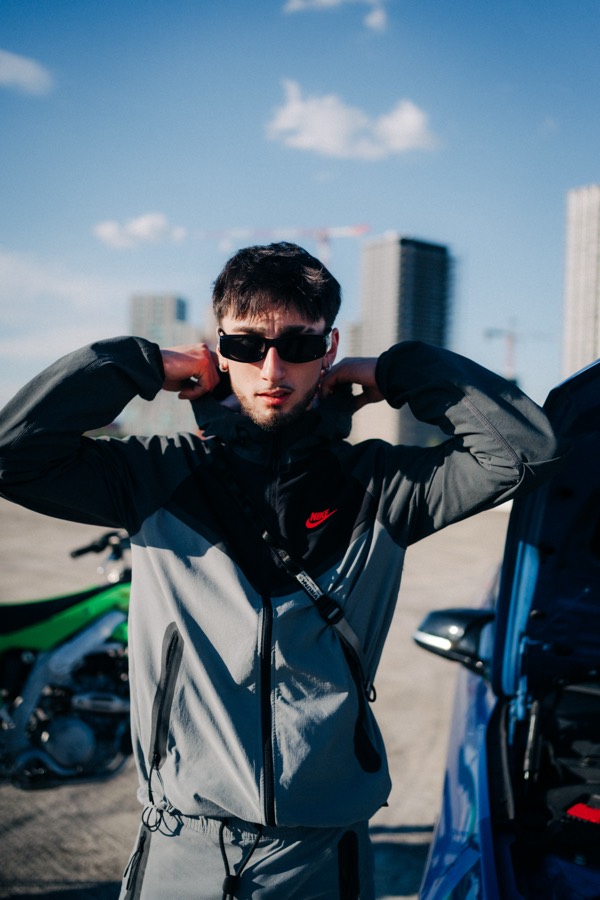Azza pulling his hood up on a rooftop, bike behind him